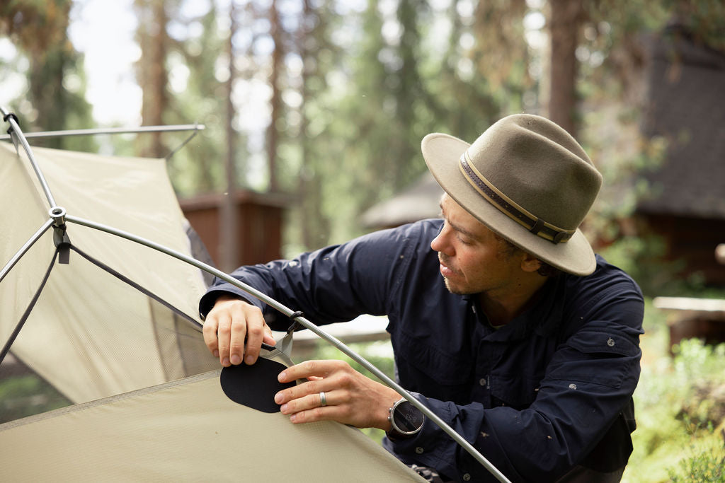 Man repairing a tent with a FabPatch Extreme patch at a forest campsite.
