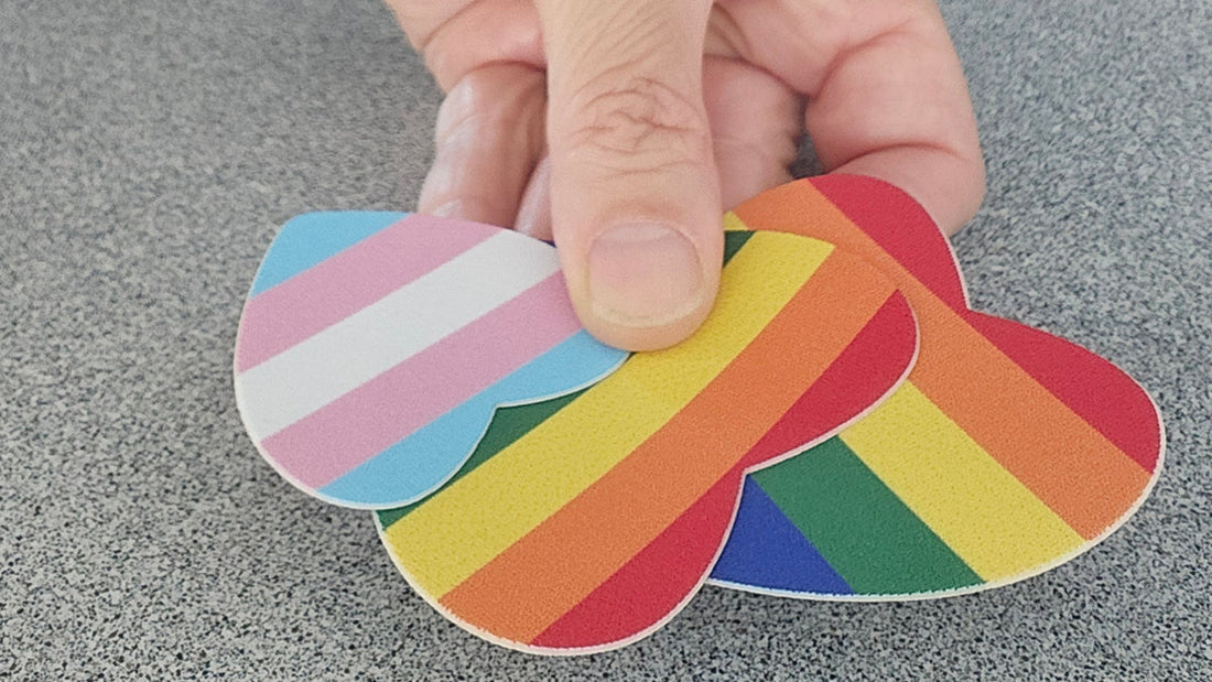 Hand holding rainbow heart-shaped FabPatch repair patches in Pride colours