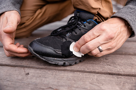 Close-up of hands applying a black FabPatch to a worn-out sneaker, demonstrating an easy and effective repair solution