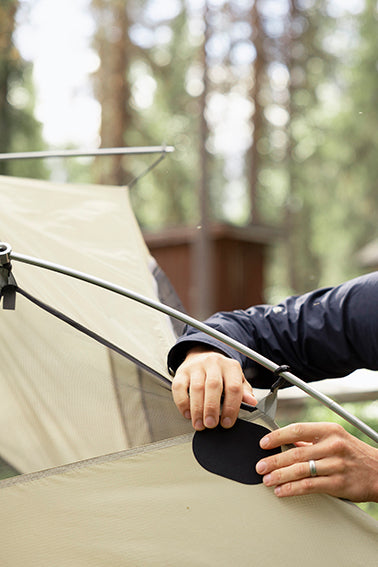 Hands repairing a tent with a black FabPatch, demonstrating a simple solution for outdoor gear maintenance during camping trips